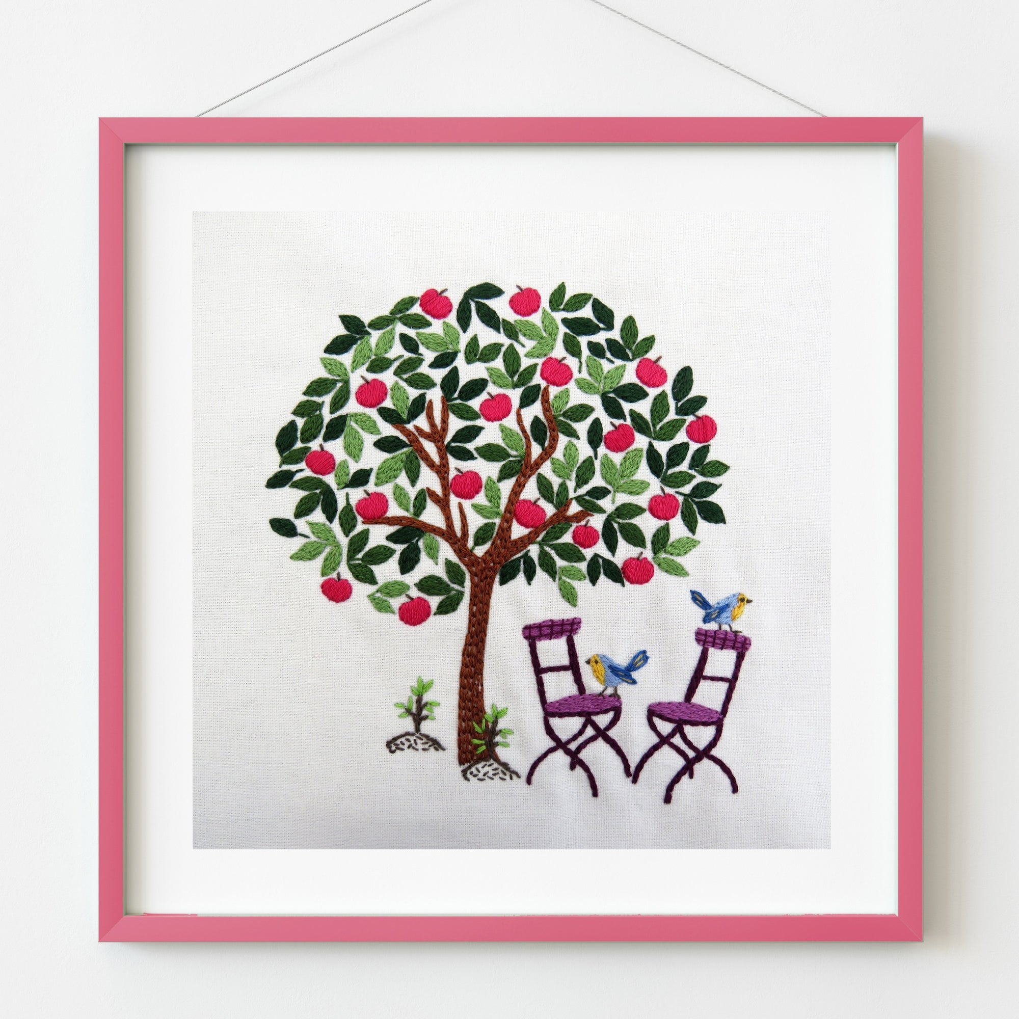 Framed artwork of a tree with birds and chairs on a white background