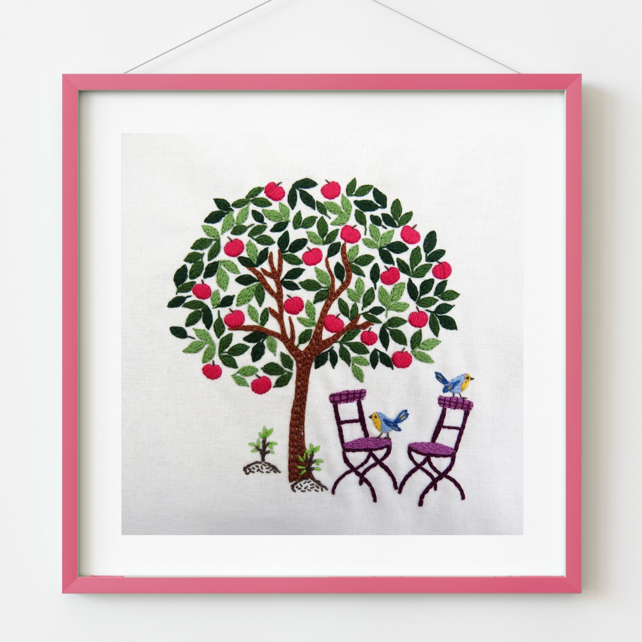 Framed artwork of a tree with birds and chairs on a white background