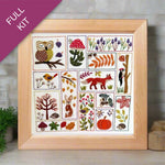 Framed embroidery kit with nature-themed designs on a wooden surface.