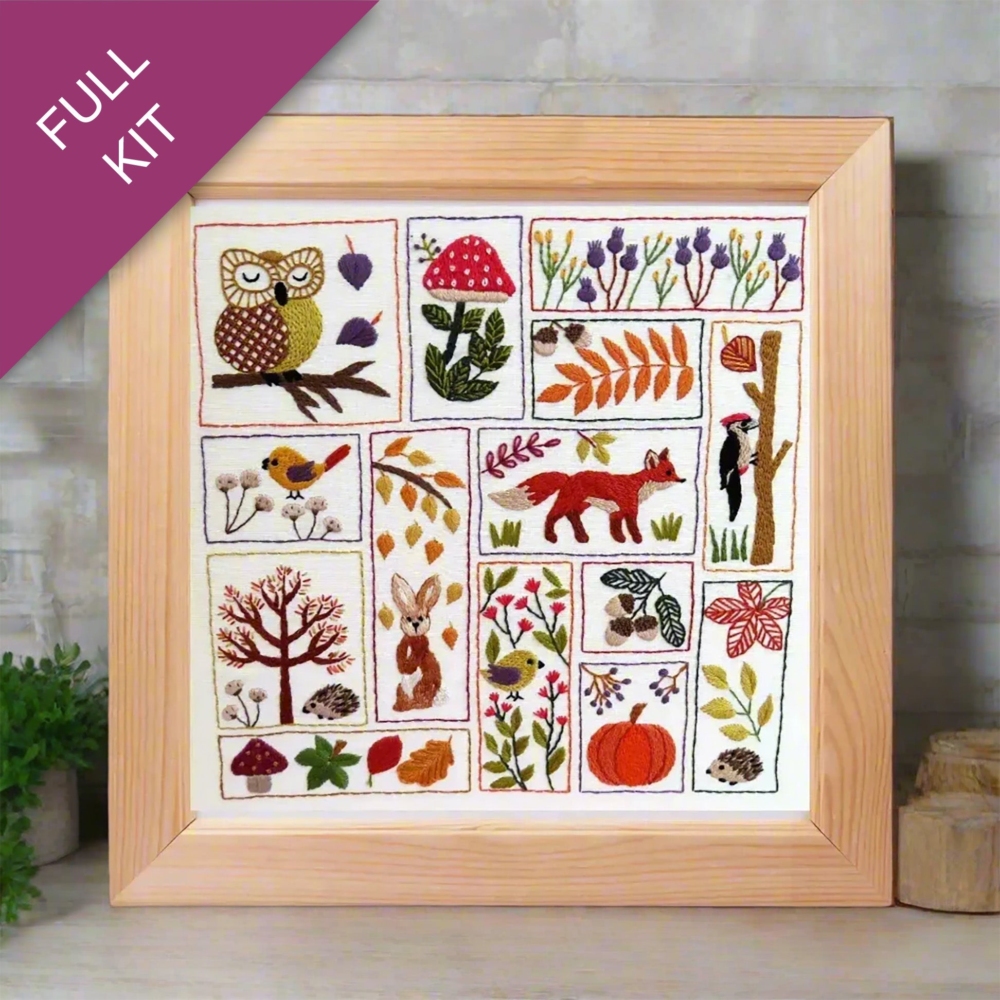Framed embroidery kit with nature-themed designs on a wooden surface.
