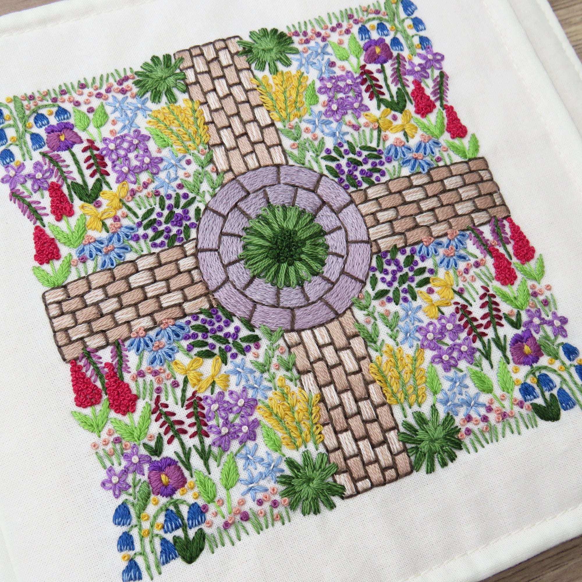Embroidered design of a garden scene with flowers and pathways on a white background