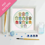 Embroidery kit with colorful beach hut design, thread, and tools on a white background.