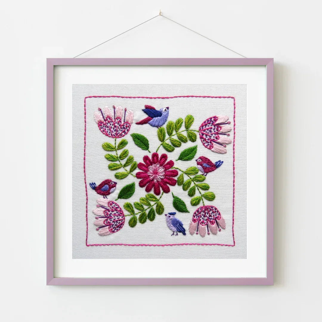 Embroidered square with flowers and birds in a pink frame on a white background