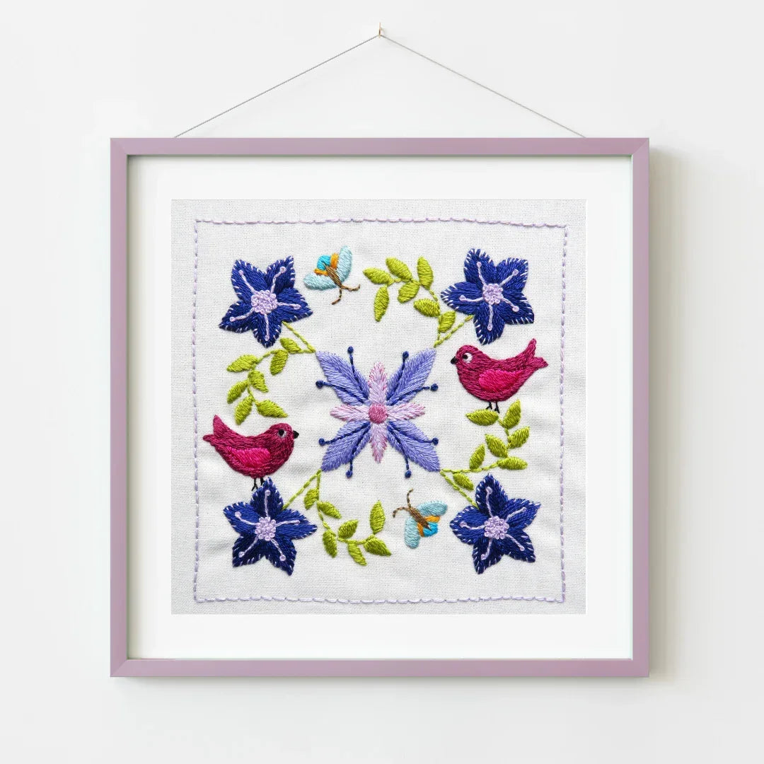 Embroidered artwork with flowers and birds in a frame on a white background