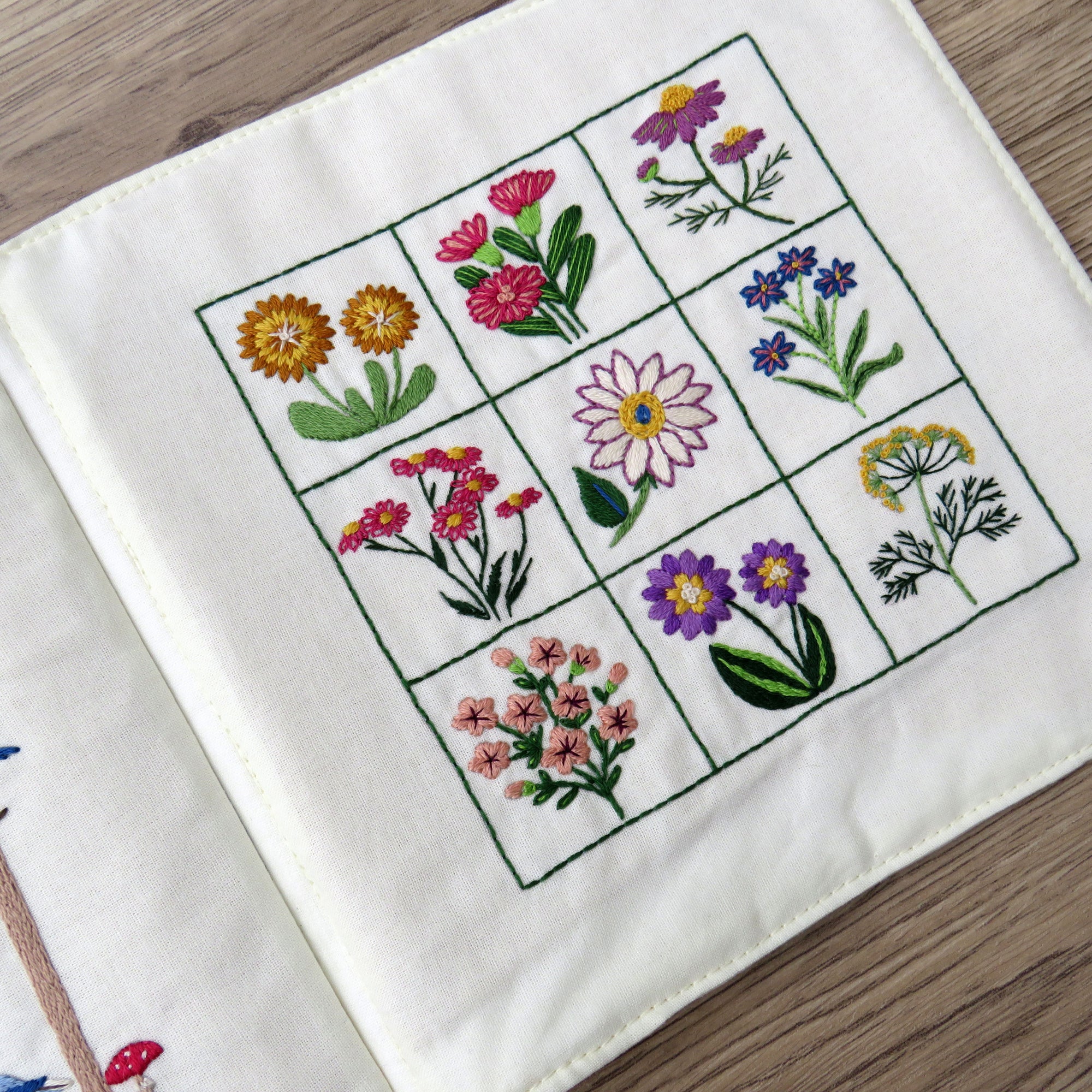 Embroidered square with various floral patterns on a white fabric background.