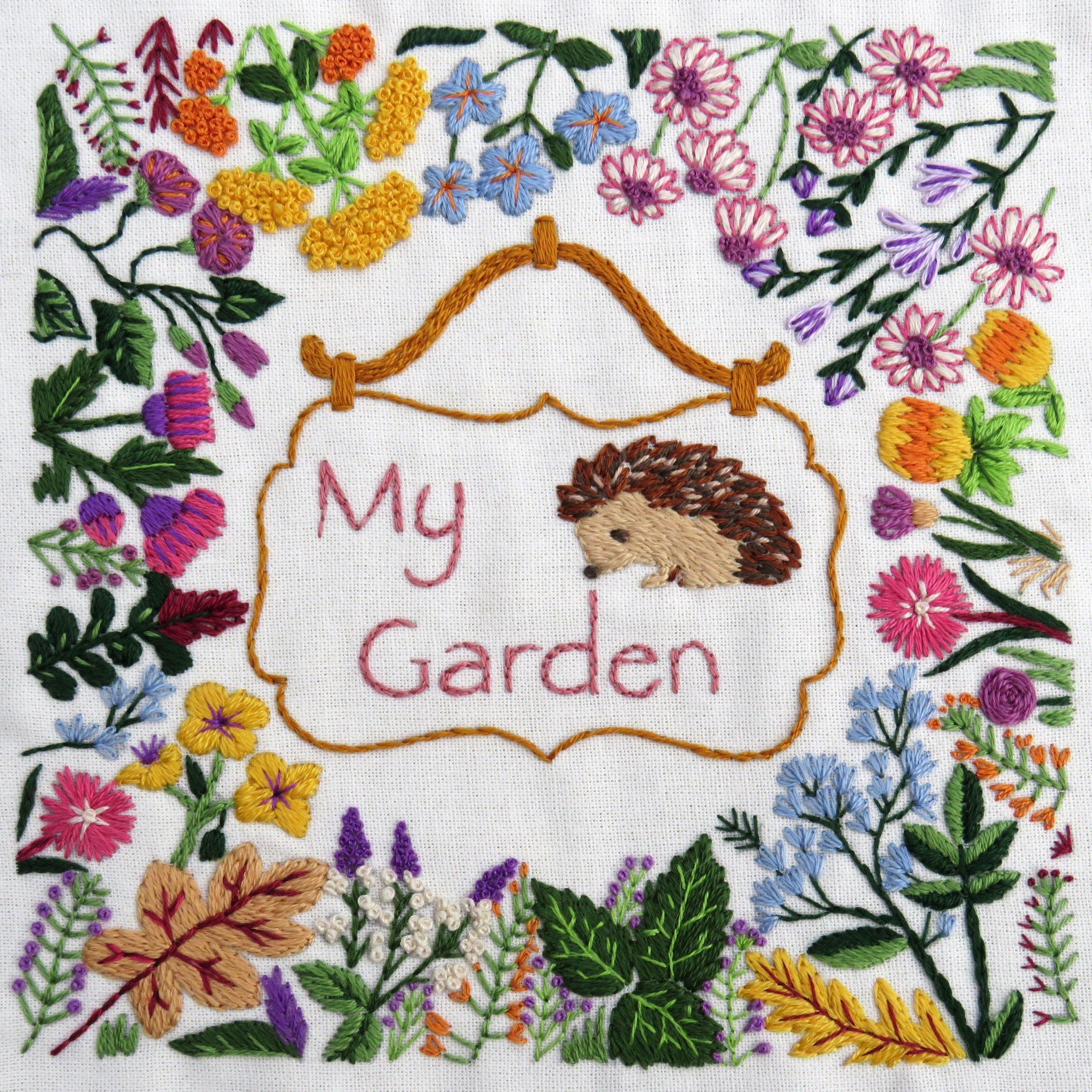Embroidered design with a hedgehog and 'My Garden' text surrounded by flowers and leaves.