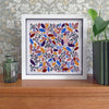 Framed artwork with colorful leaf pattern on a wooden surface with decorative background