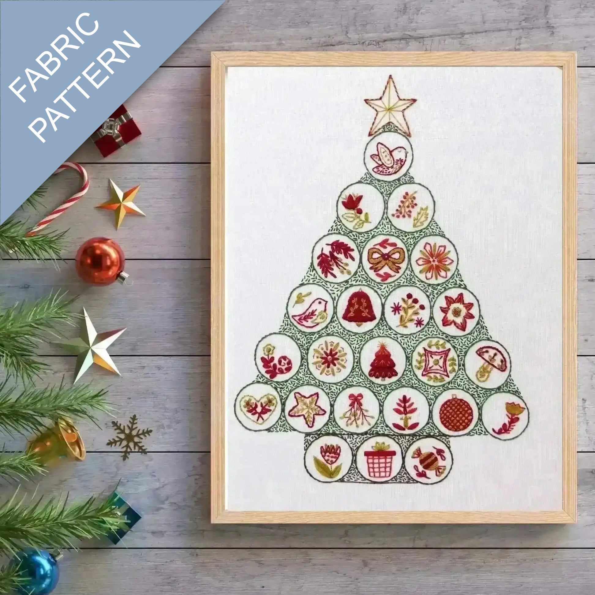 Framed fabric pattern with Christmas tree design on a wooden surface with festive decorations.