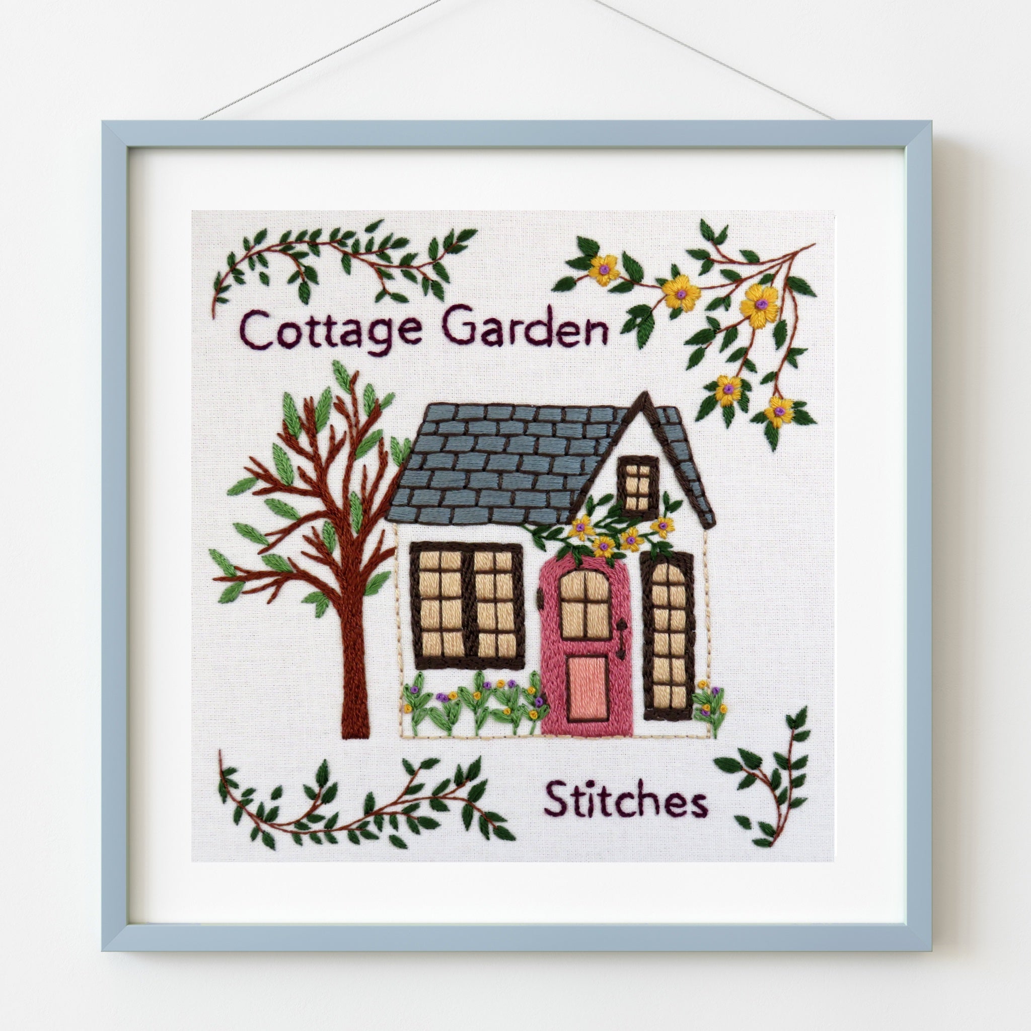 Embroidery of a cottage with 'Cottage Garden Stitches' text, framed in light blue.