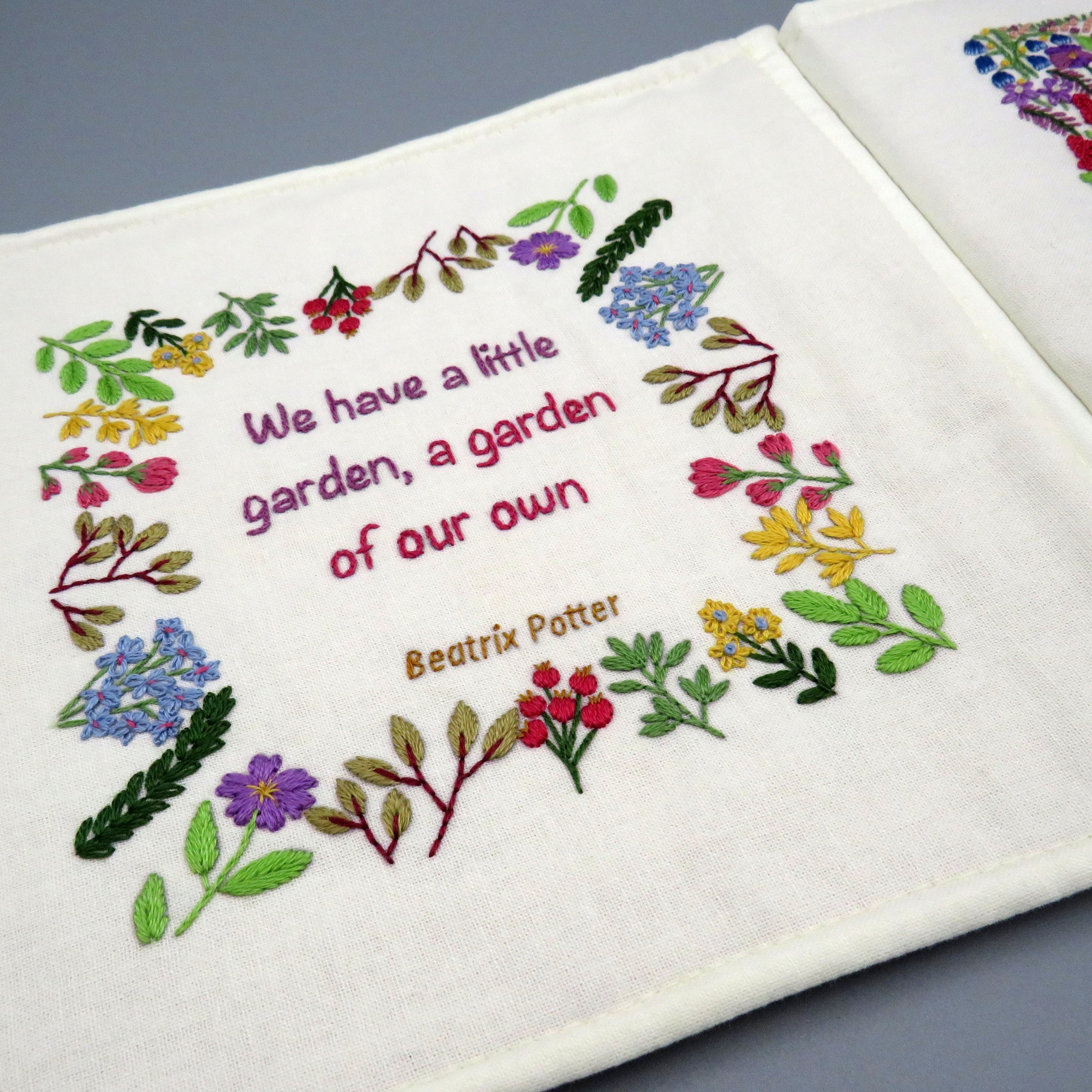 Embroidered text and floral design on a white fabric with a gray background