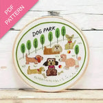 Embroidery hoop with 'Dog Park' design featuring cartoon dogs and trees on a wooden surface.