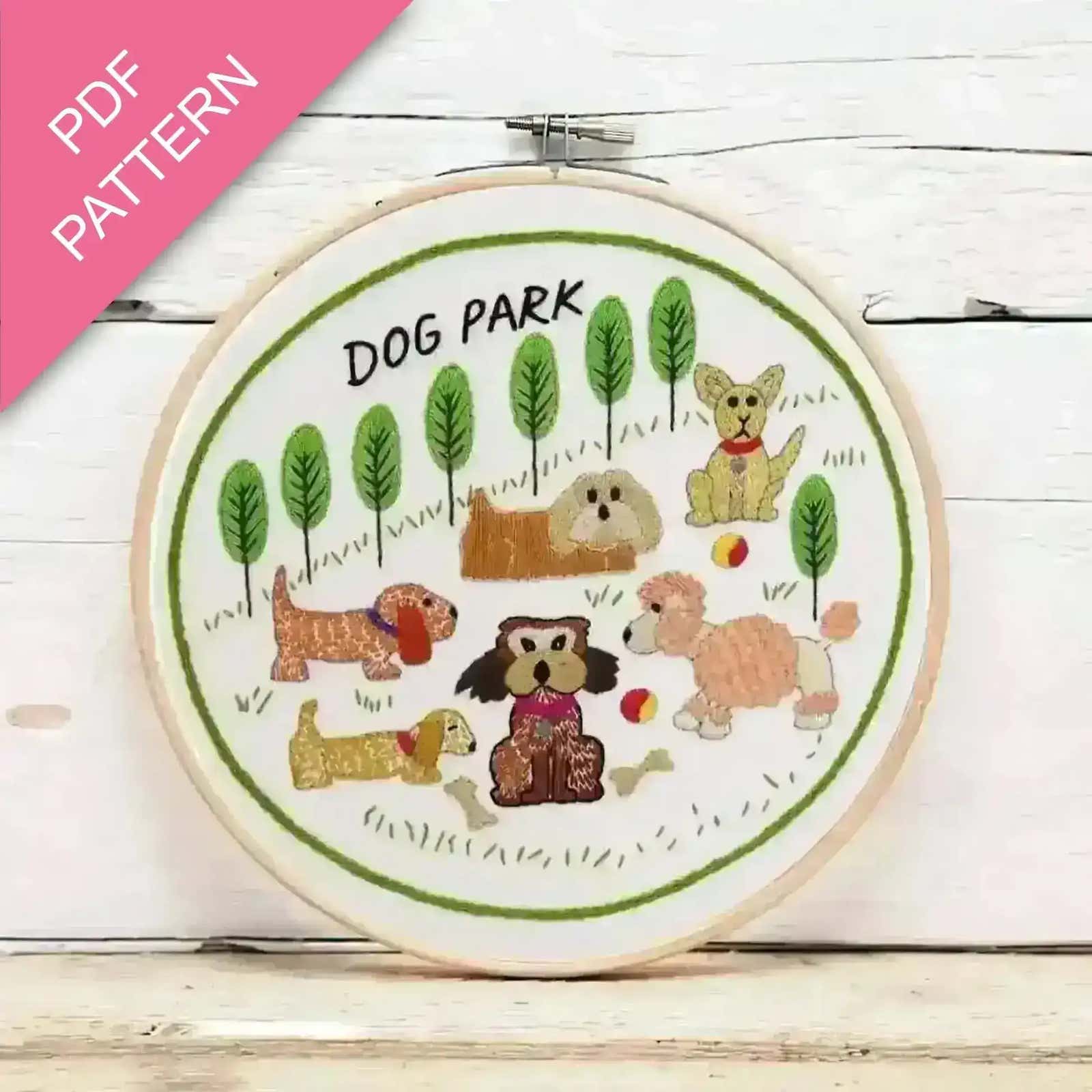 Embroidery hoop with 'Dog Park' design featuring cartoon dogs and trees on a wooden surface.