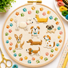 Embroidery hoop with embroidered dogs and paw prints on a white surface with embroidery supplies.