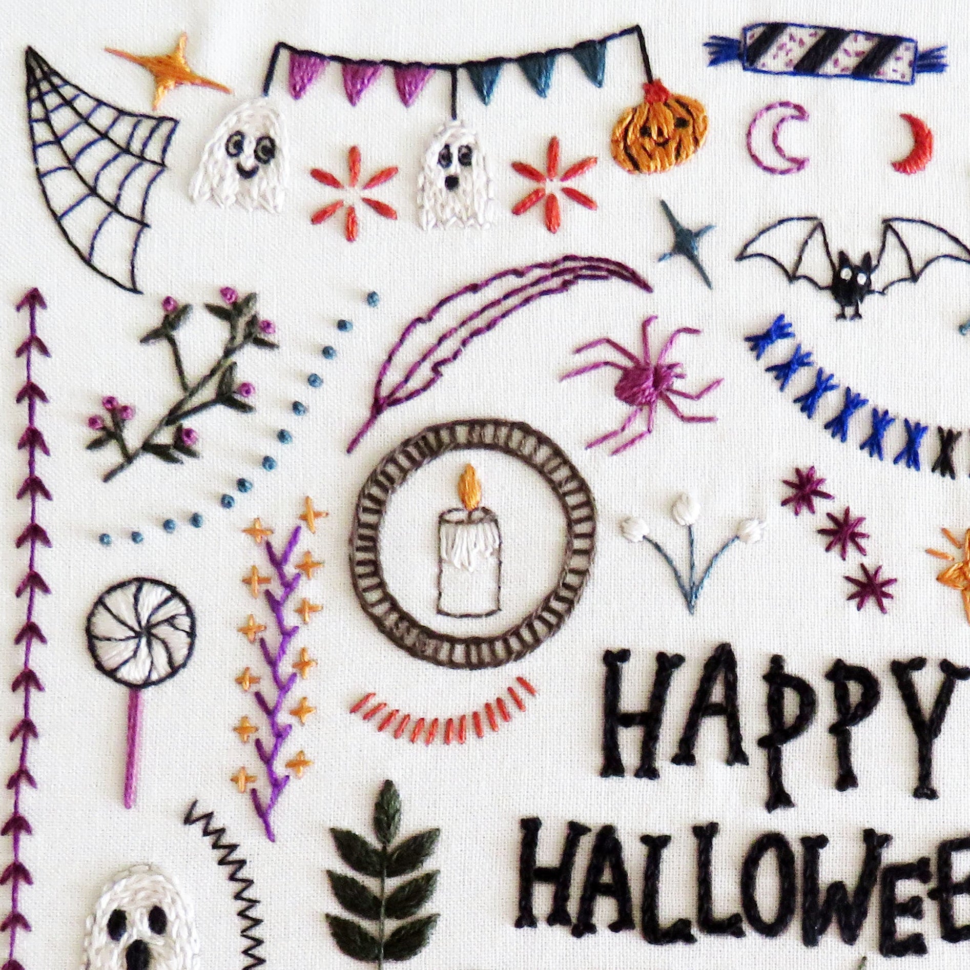 A square white fabric or paper sample featuring a dense collection of colorful Halloween-themed embroidered motifs, including 'HAPPY HALLOWEEN' text, cobwebs, ghosts, pumpkins, bats, spiders, a witch hat, a cat, and decorative banners.