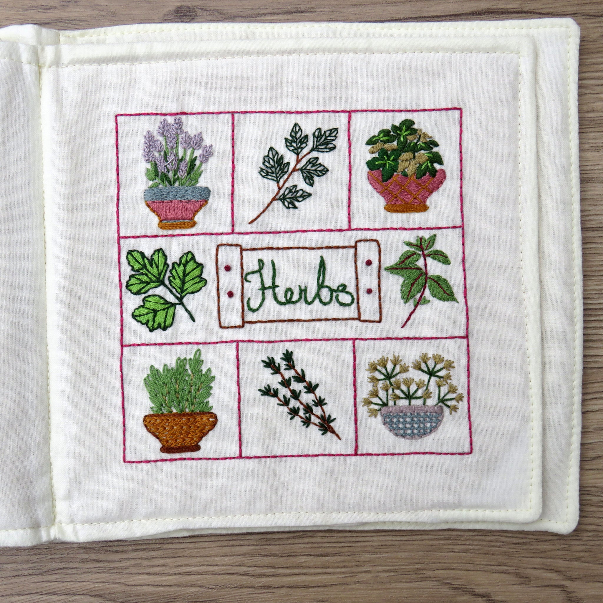 Embroidered potholder with herb designs on a wooden surface