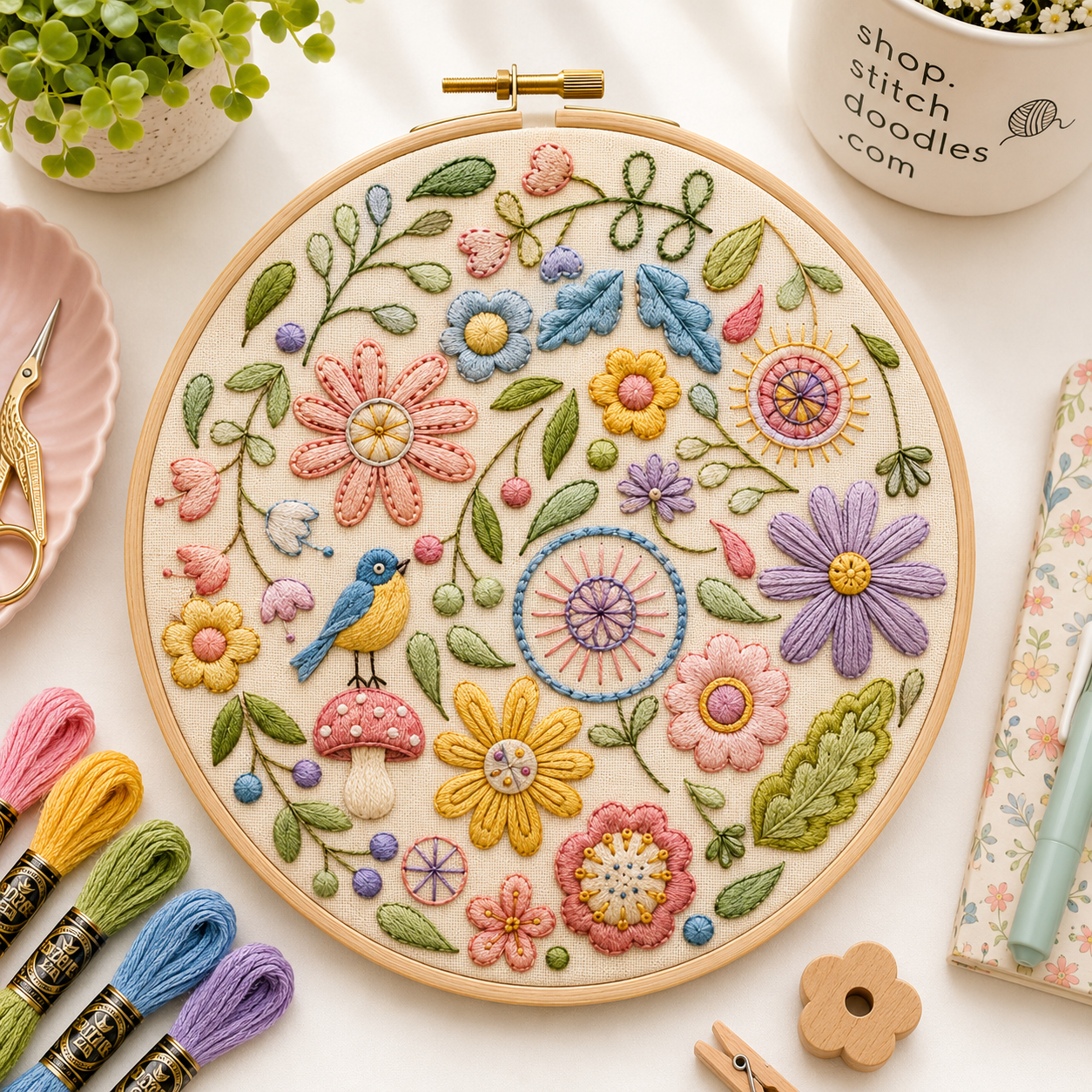 Embroidery hoop with colorful floral design on a table with embroidery supplies.