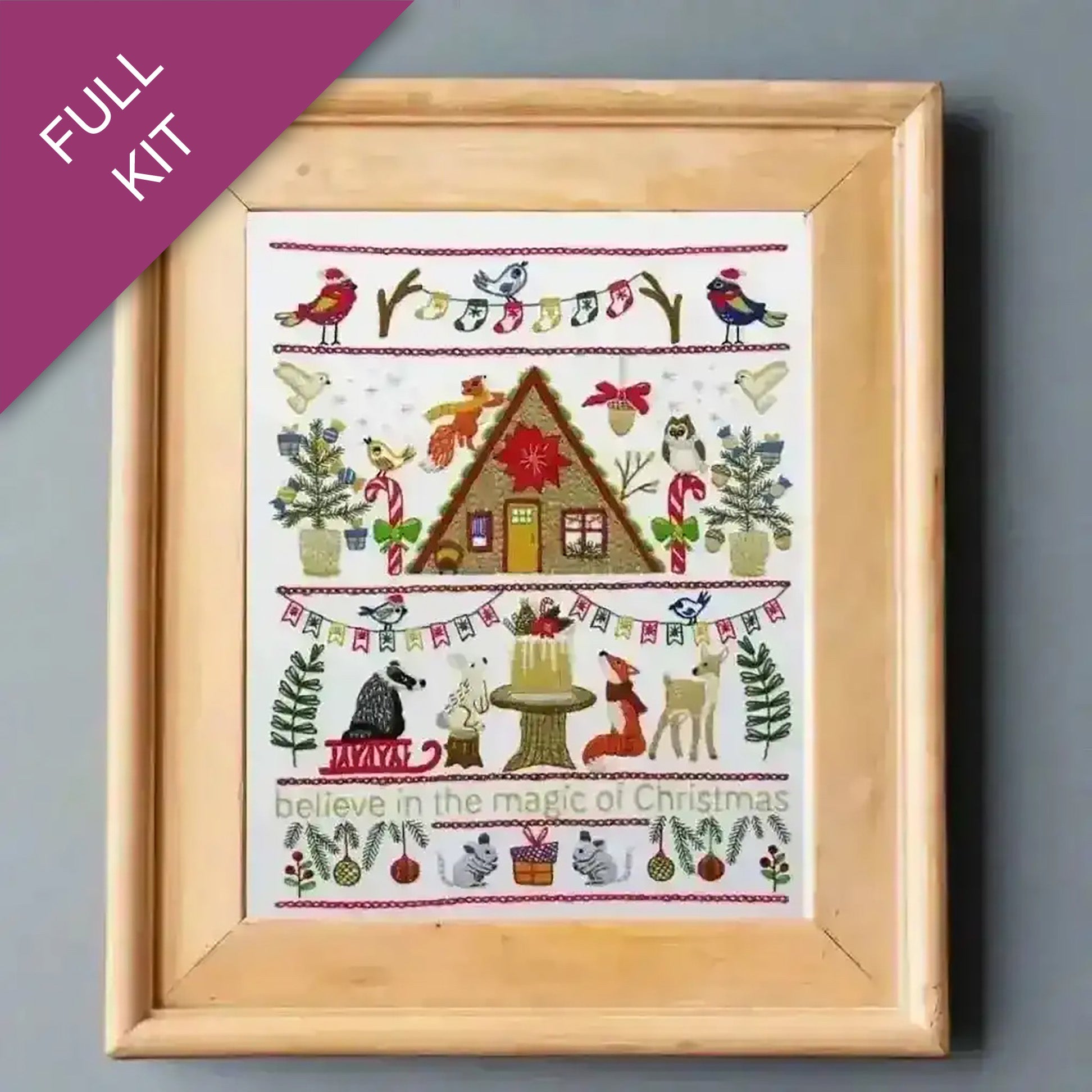 Framed cross-stitch kit with Christmas-themed design on a gray background
