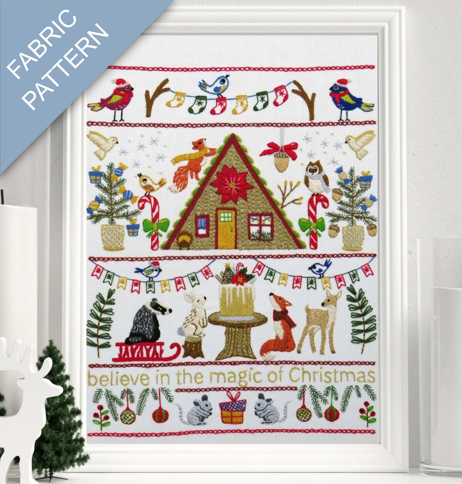 Framed fabric pattern with Christmas-themed design featuring a cabin, animals, and festive elements.