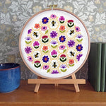 Embroidery hoop with floral and bee pattern on a wooden stand against a decorative wall.