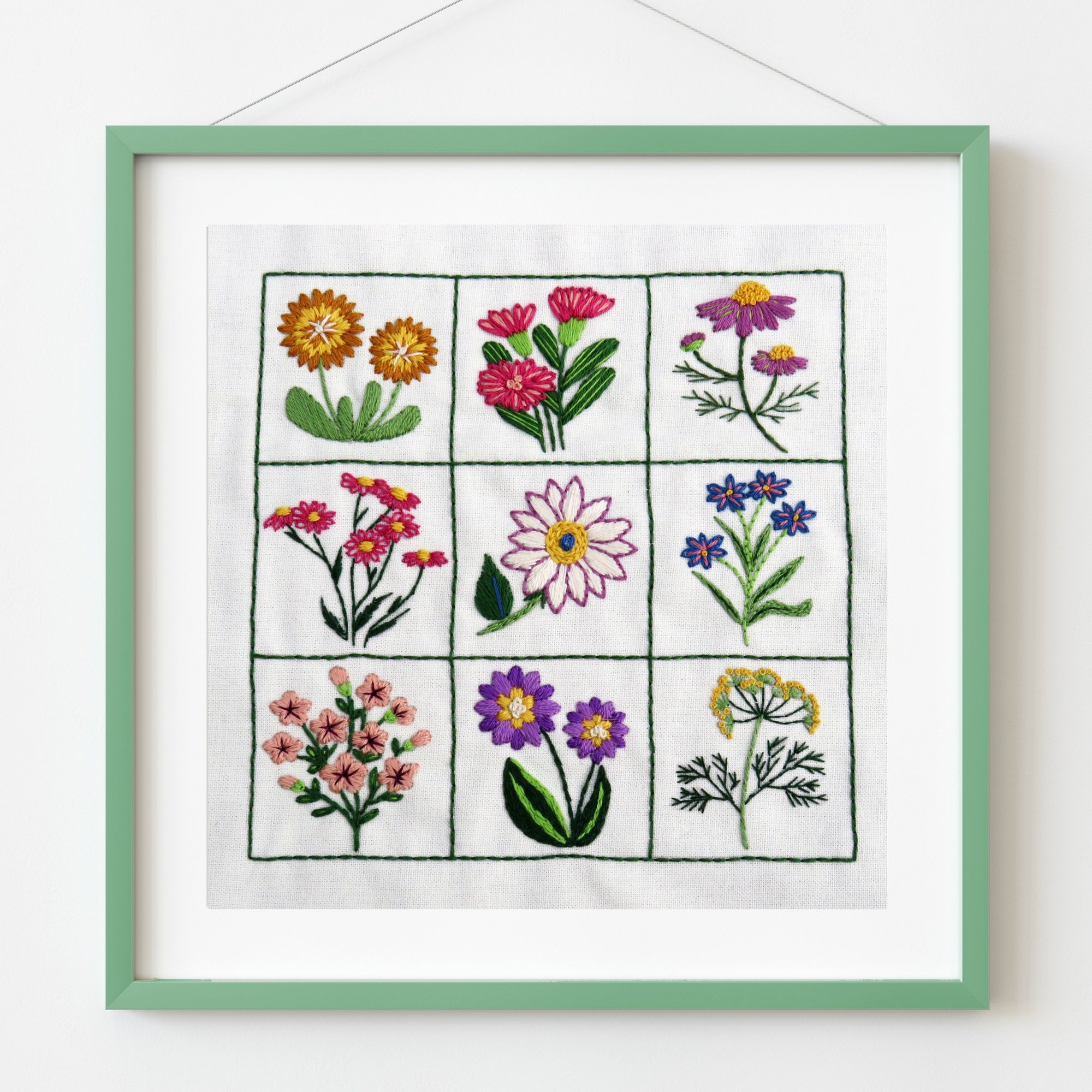 Framed embroidery of various flowers on a white background
