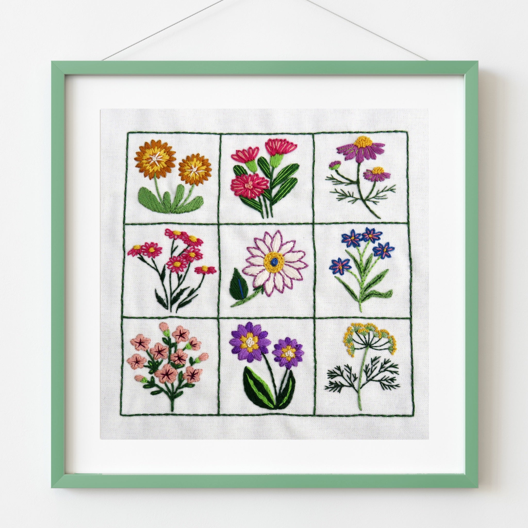 Framed embroidery of various flowers on a white background