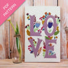 Embroidery pattern with 'LOVE' letters and floral designs on a wooden surface.