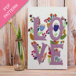Embroidery pattern with 'LOVE' letters and floral designs on a wooden surface.