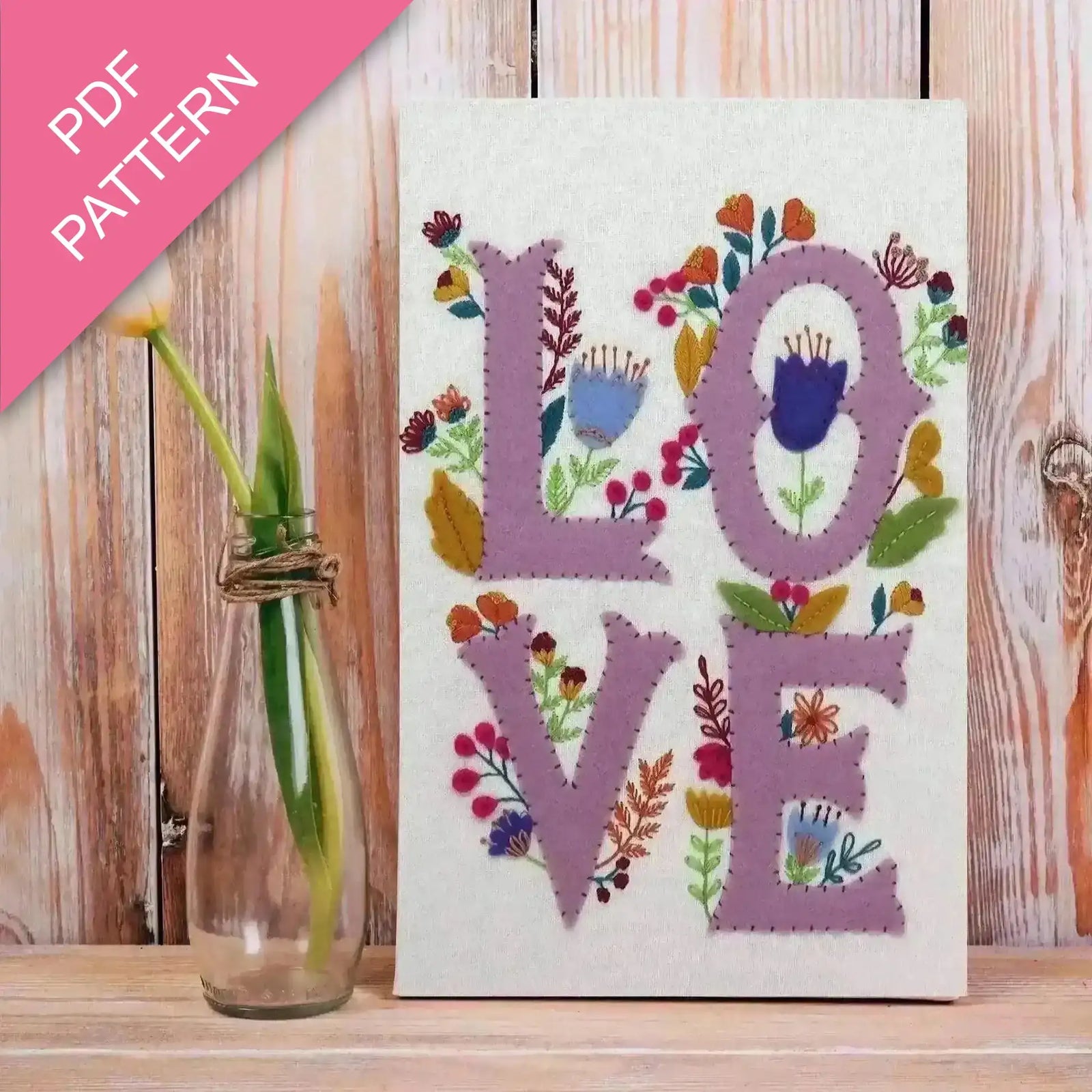 Embroidery pattern with 'LOVE' letters and floral designs on a wooden surface.