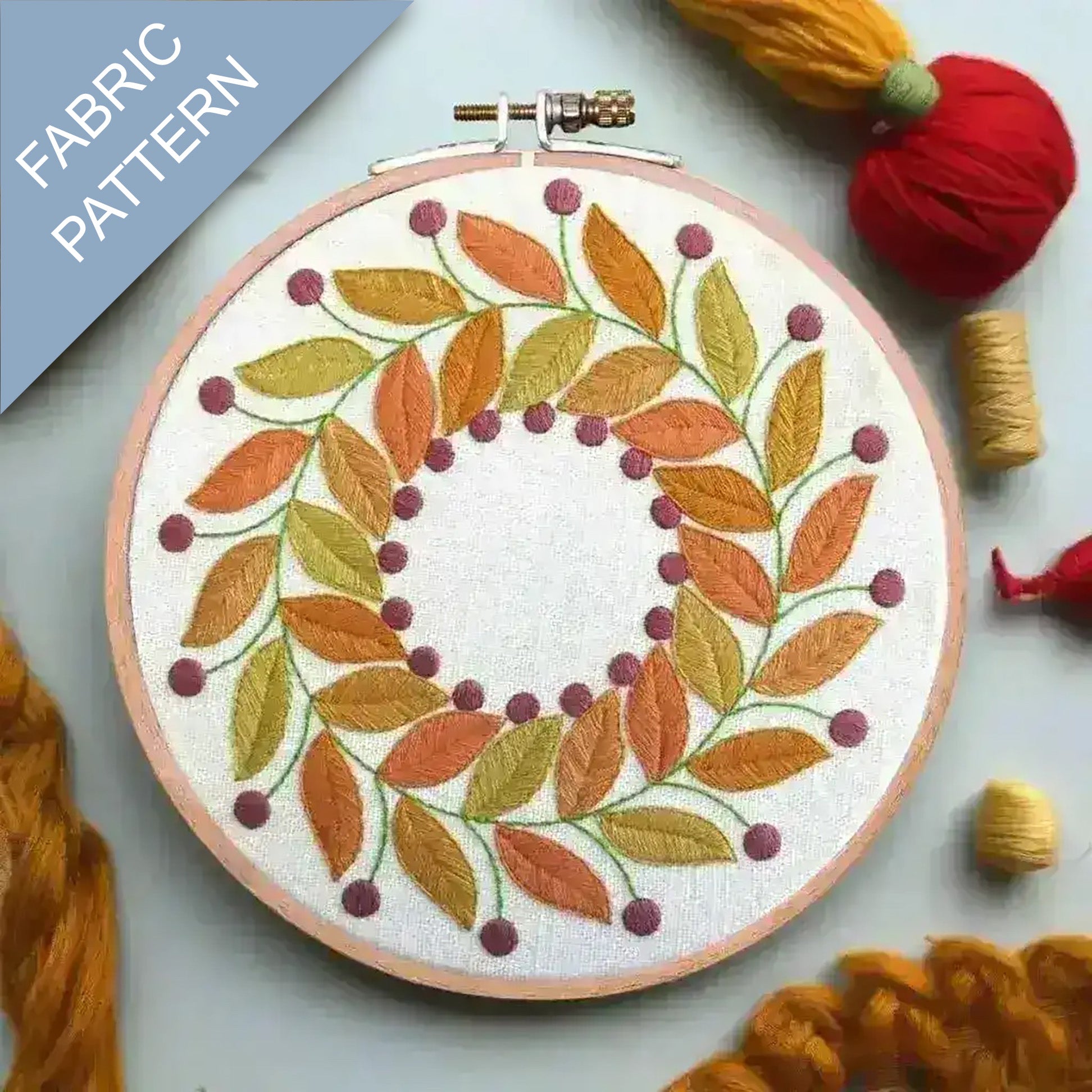 Embroidery hoop with autumn leaf pattern surrounded by yarn and fabric