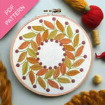 Embroidery hoop with autumn leaf pattern surrounded by yarn on a light background