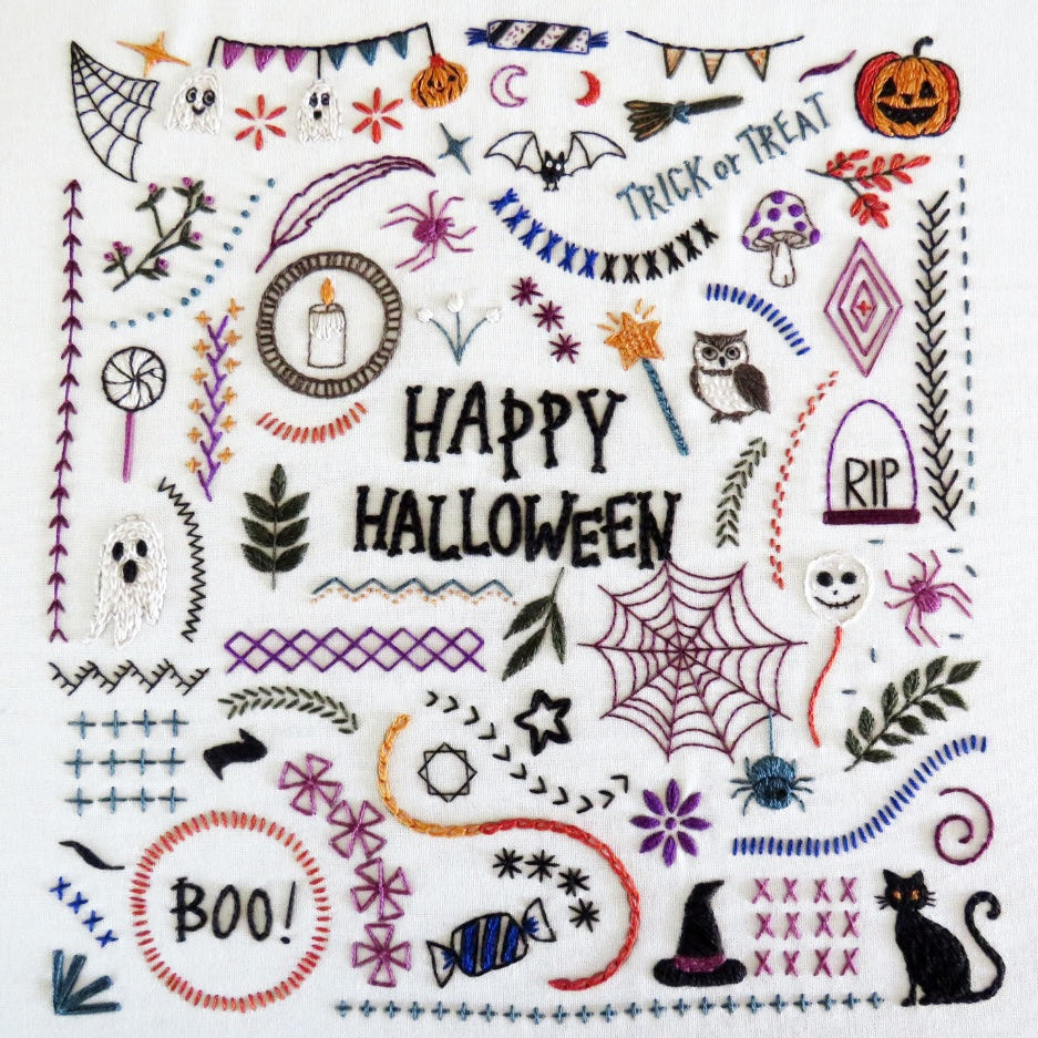 A square white fabric patch or sampler featuring colorful embroidered Halloween motifs and the words “HAPPY HALLOWEEN” in the center, surrounded by spiders, ghosts, pumpkins, bats, stars, banners, and decorative stitched patterns.