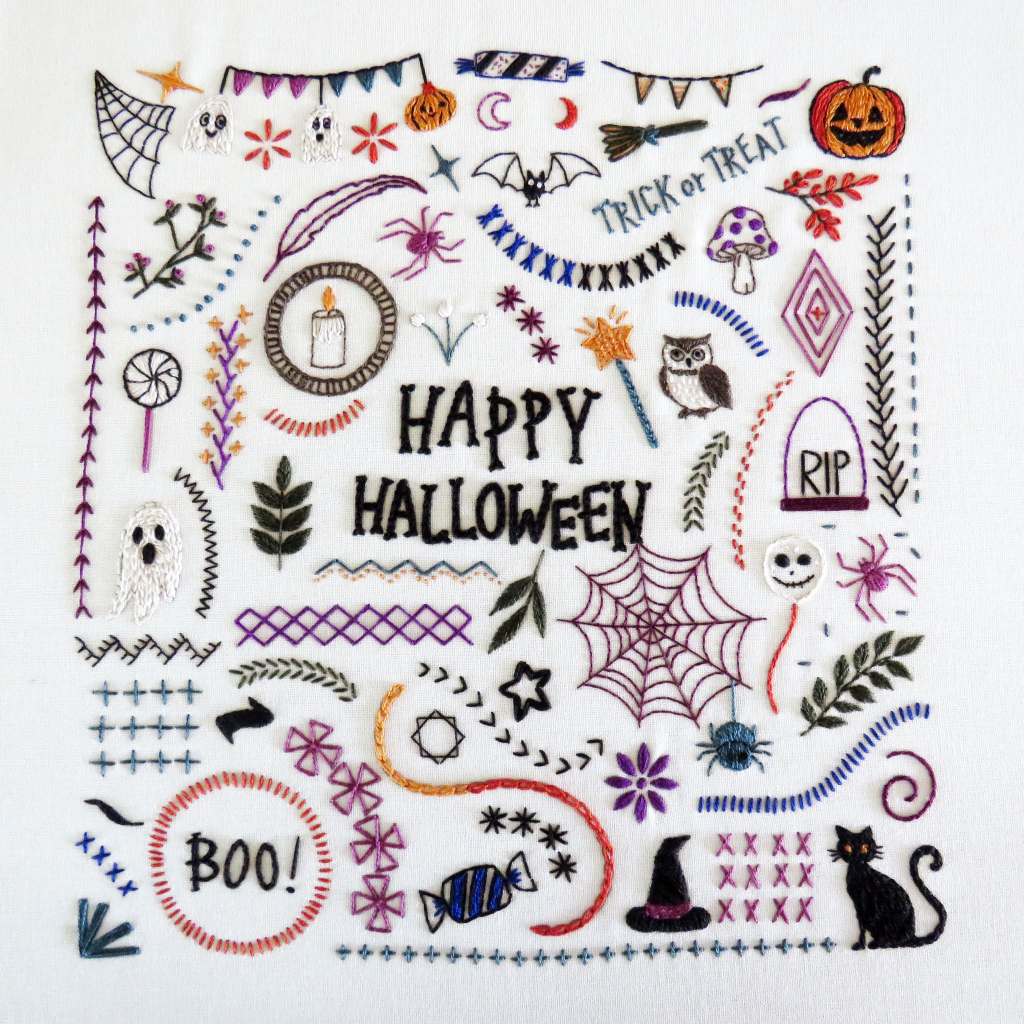 A square white fabric patch featuring colorful embroidered Halloween-themed designs and the words “HAPPY HALLOWEEN” in the center, surrounded by spiders, ghosts, pumpkins, bats, stars, banners, and decorative stitched borders.
