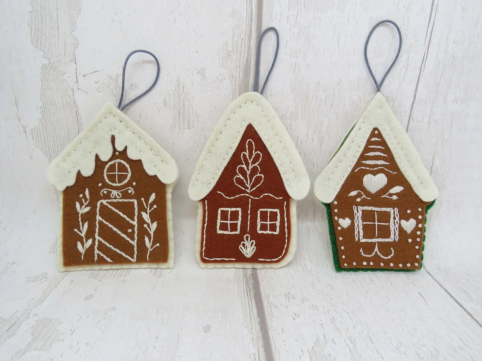 Three gingerbread house-shaped ornaments on a wooden surface