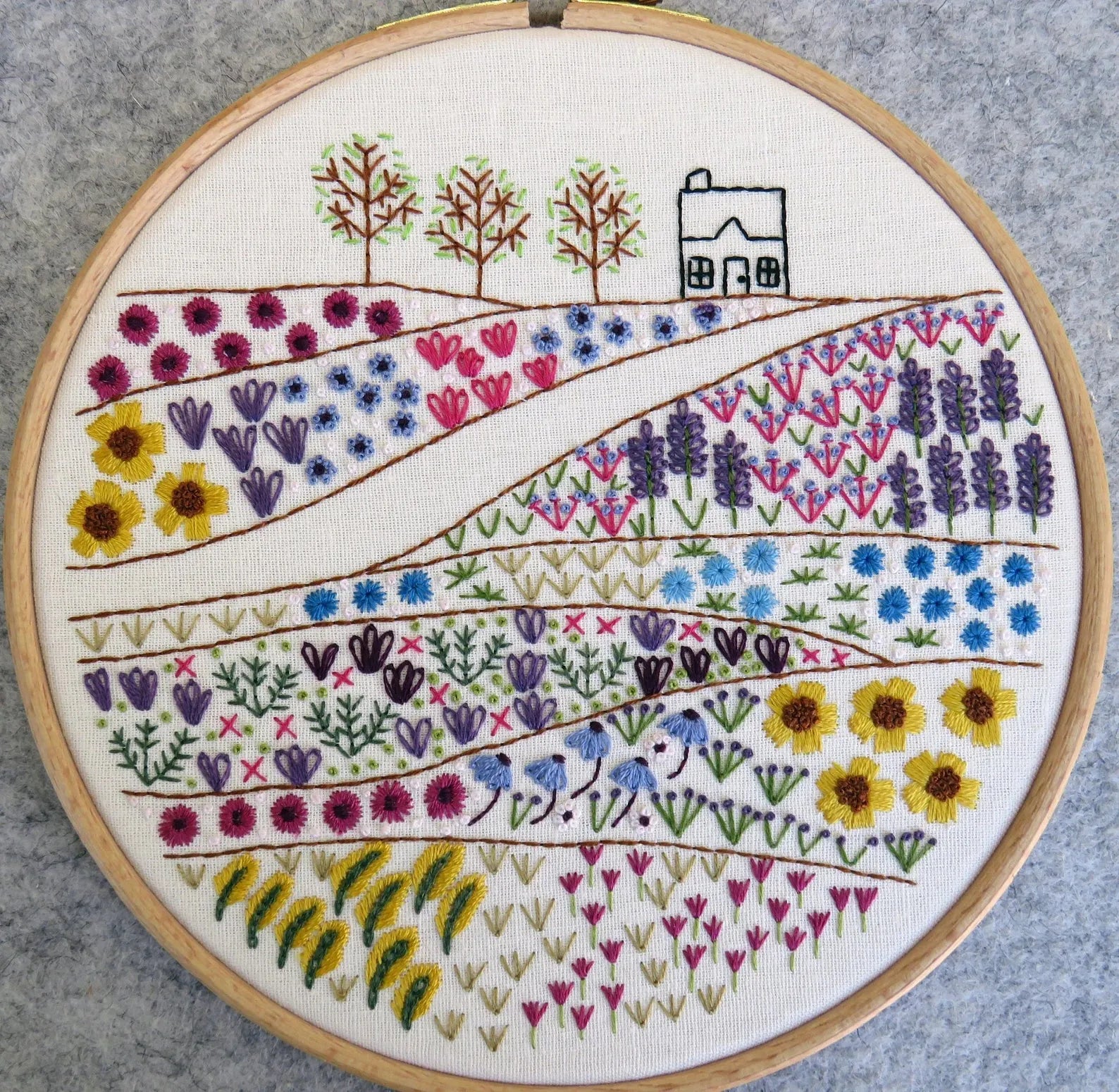 Embroidery hoop with floral and landscape design on a gray background