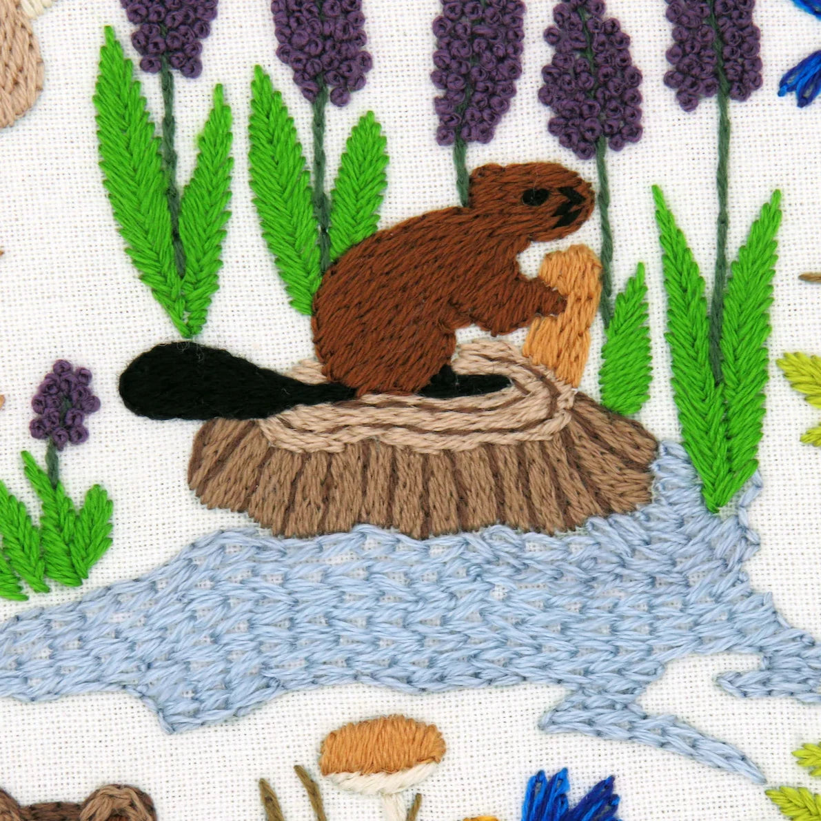 Embroidered design of a beaver on a log with plants and mushrooms