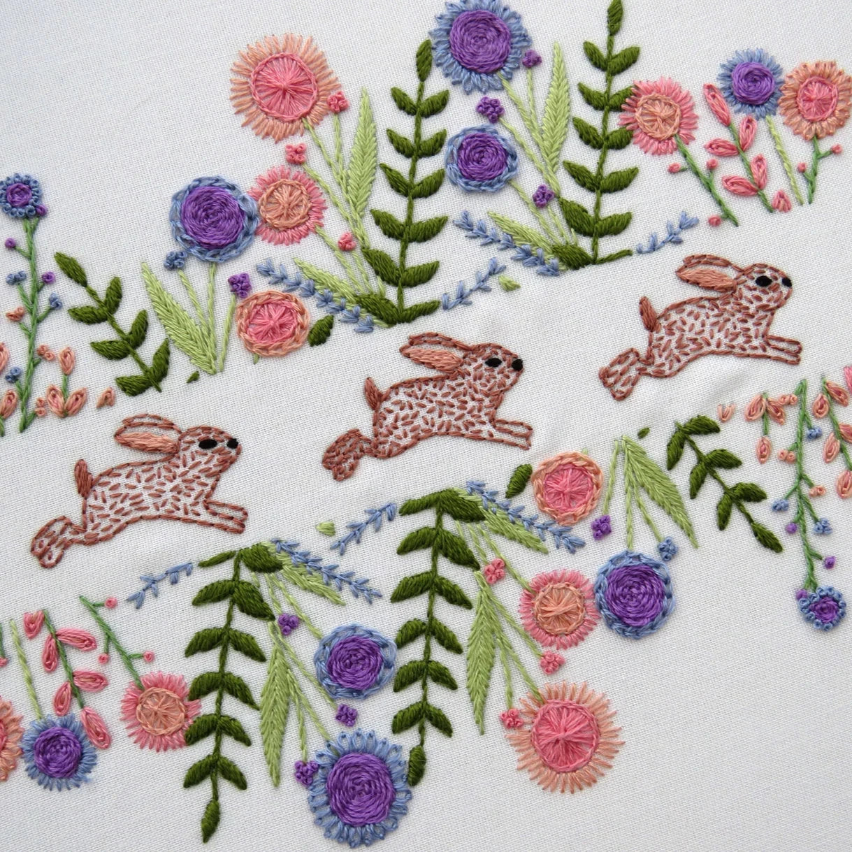 Embroidery design with rabbits and flowers on a white background