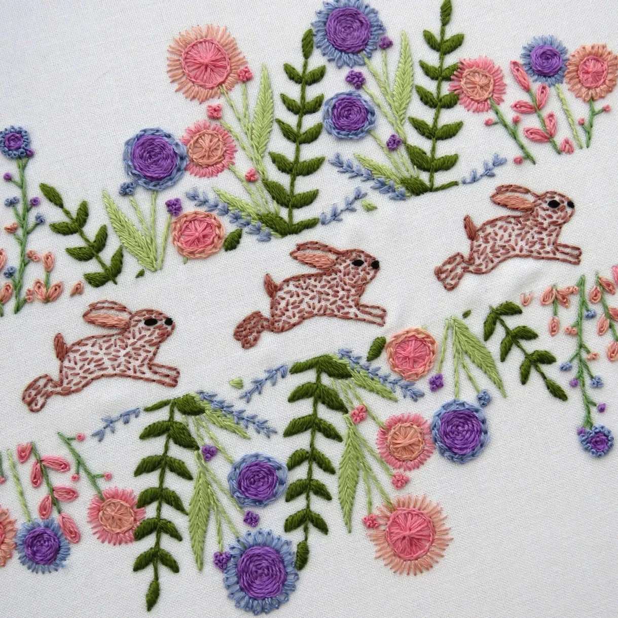 Embroidery design with rabbits and flowers on a white background