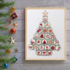 Framed Christmas tree art print with decorative elements on a wooden surface.