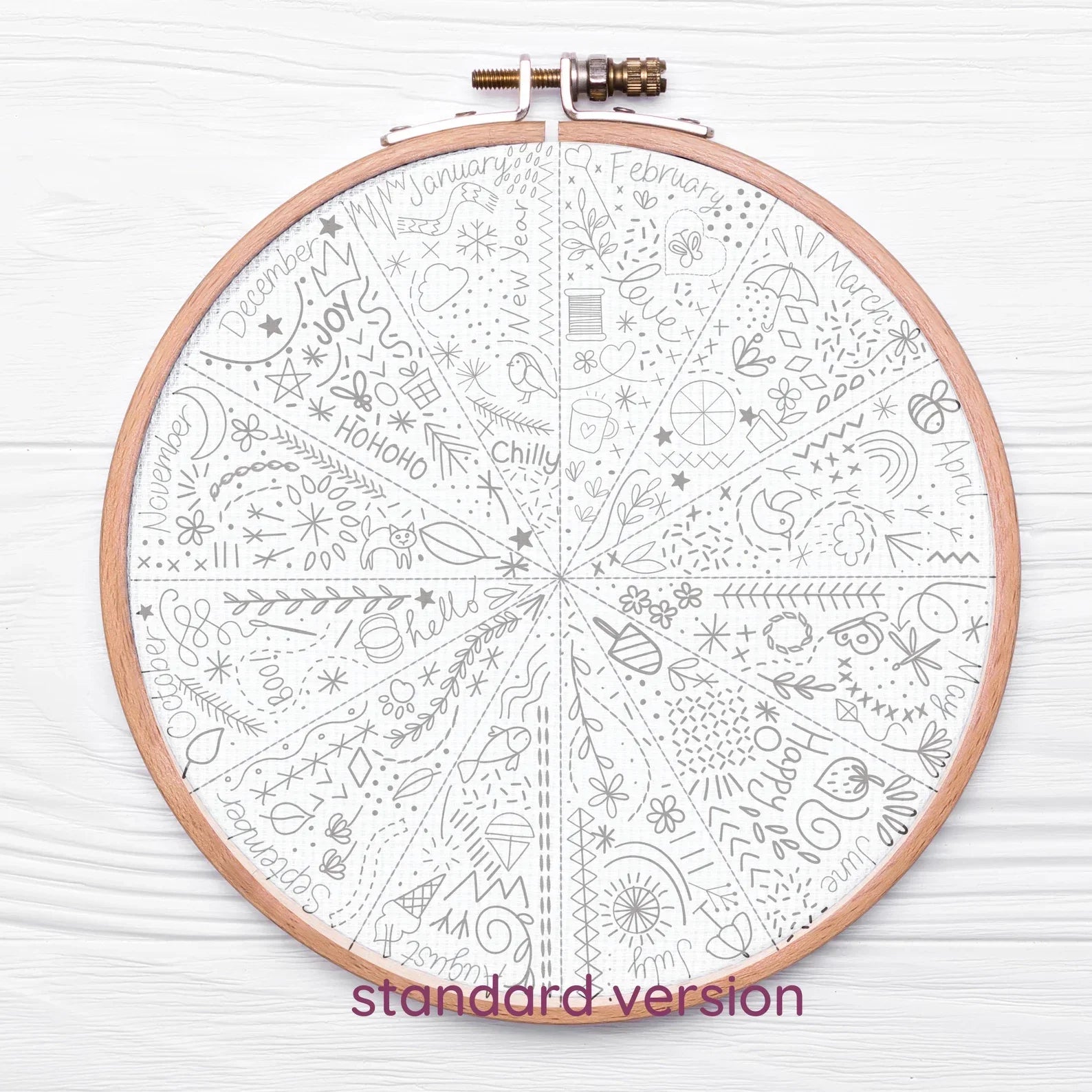 Embroidery hoop with a white fabric featuring black patterns on a light wooden surface.