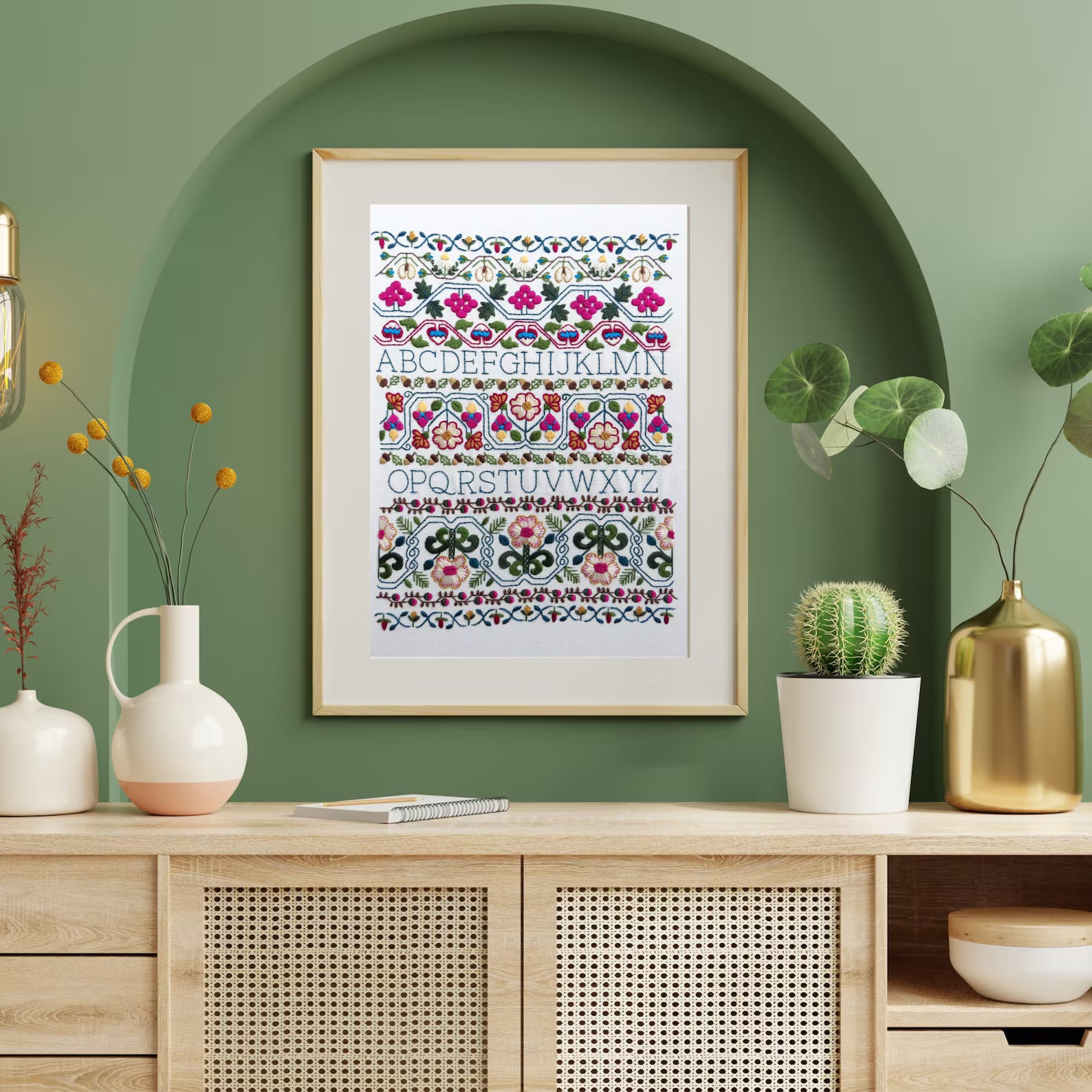 Framed colorful alphabet print on a green wall with decorative vases and plants.