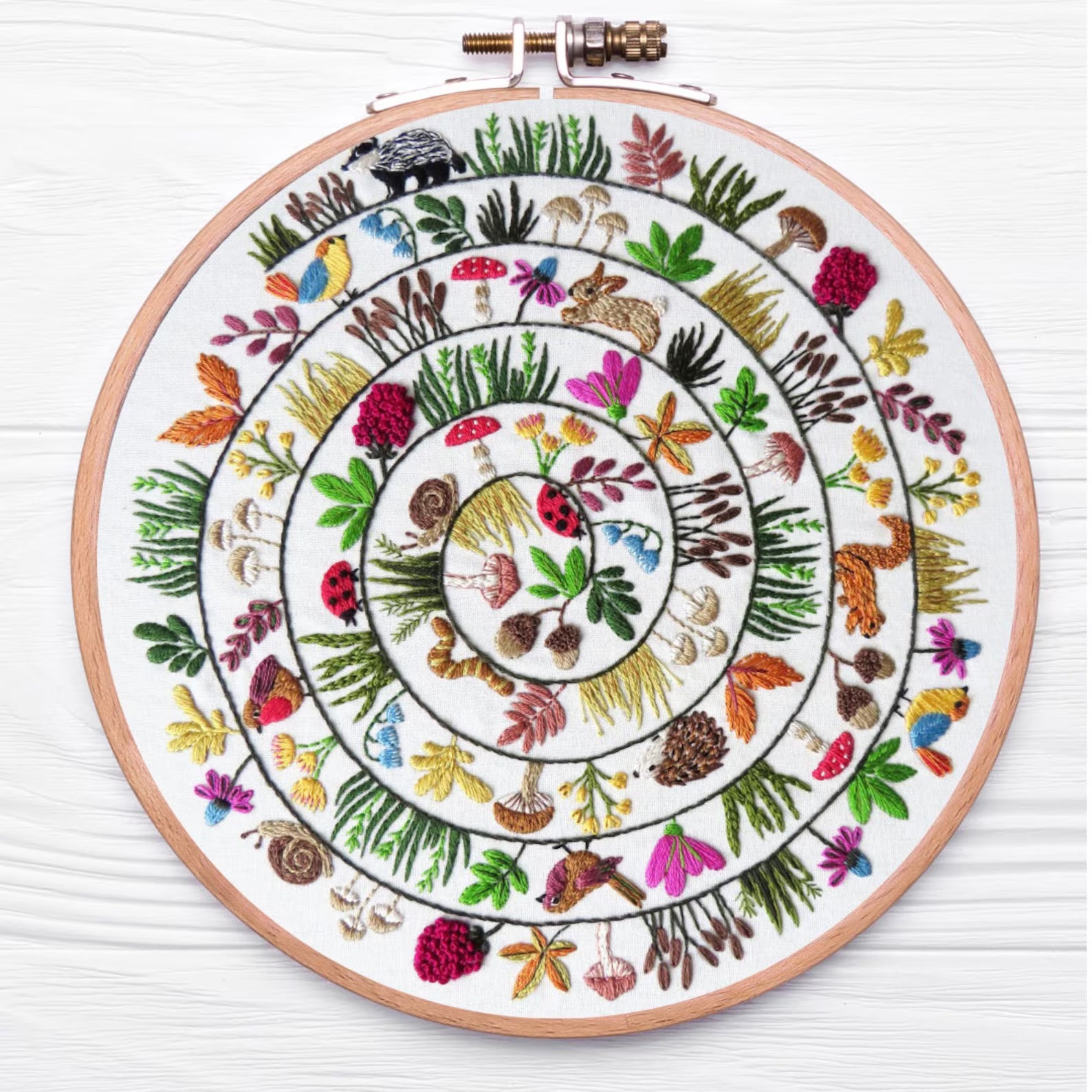 Embroidery hoop with a colorful floral and nature-themed design on a white background