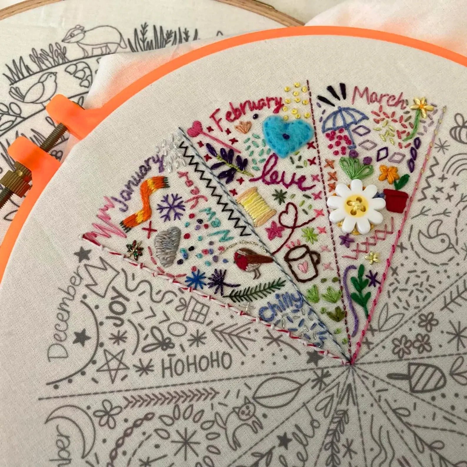 Embroidery hoop with colorful embroidered design featuring months of the year and floral elements.