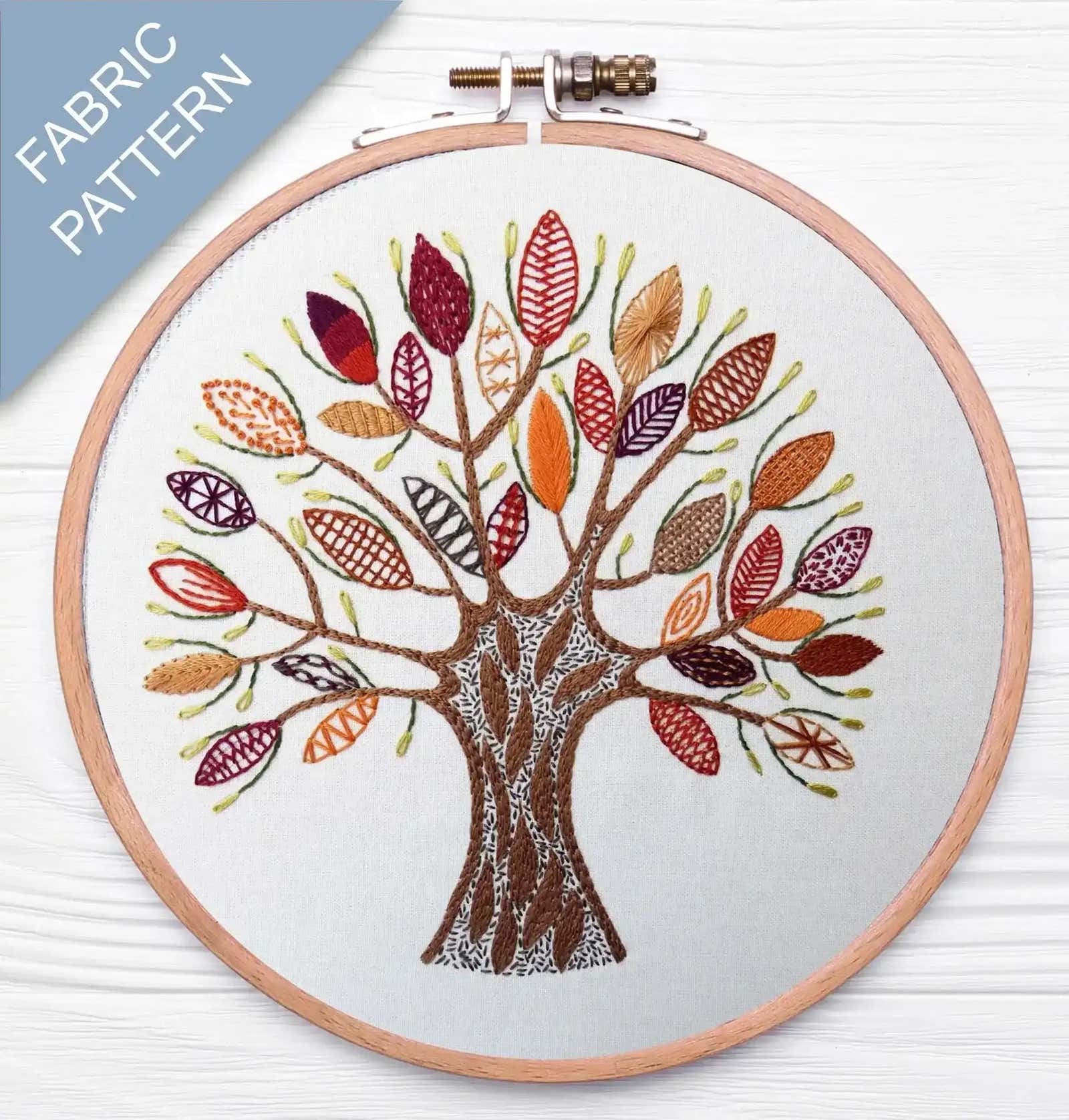 Embroidery hoop with a tree design featuring colorful leaves on a white background.