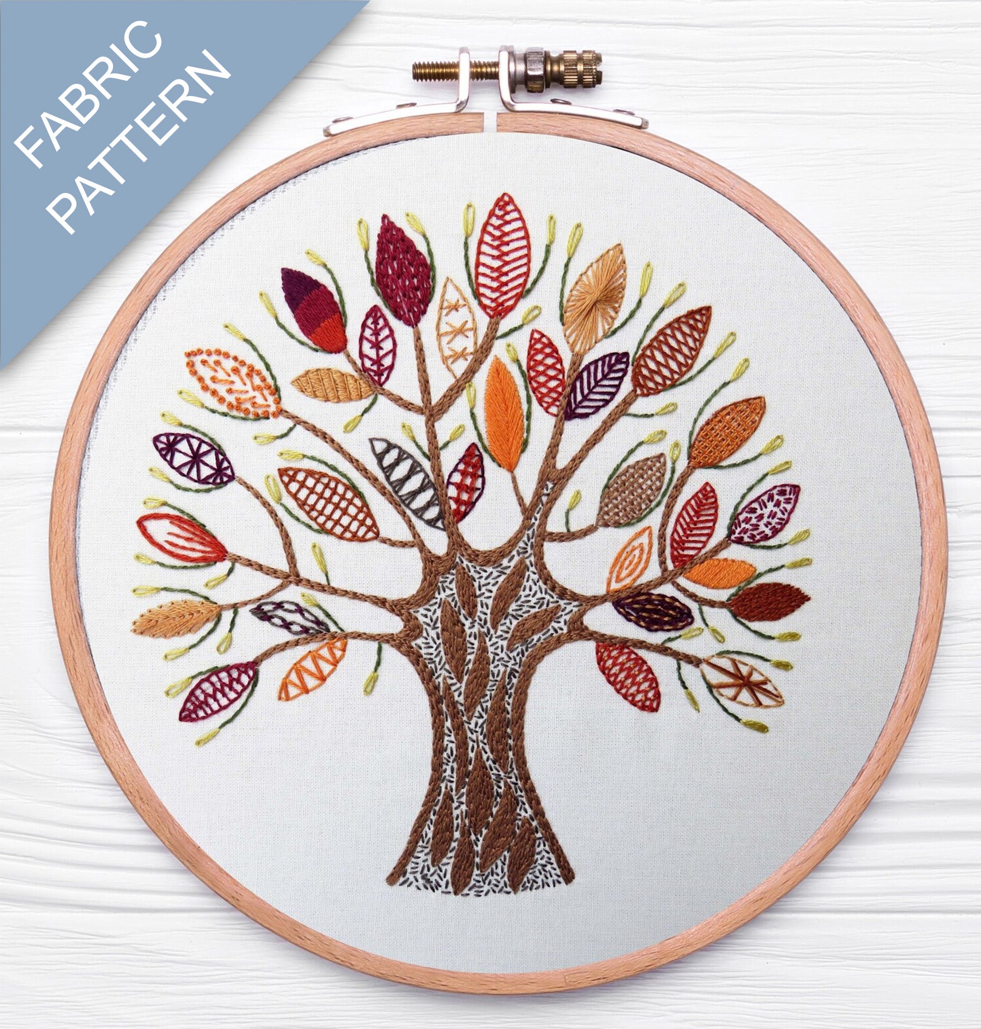 Embroidery hoop with a tree design featuring colorful leaves on a white background.