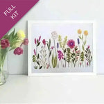 Framed artwork of colorful flowers next to a vase with real flowers on a white surface.