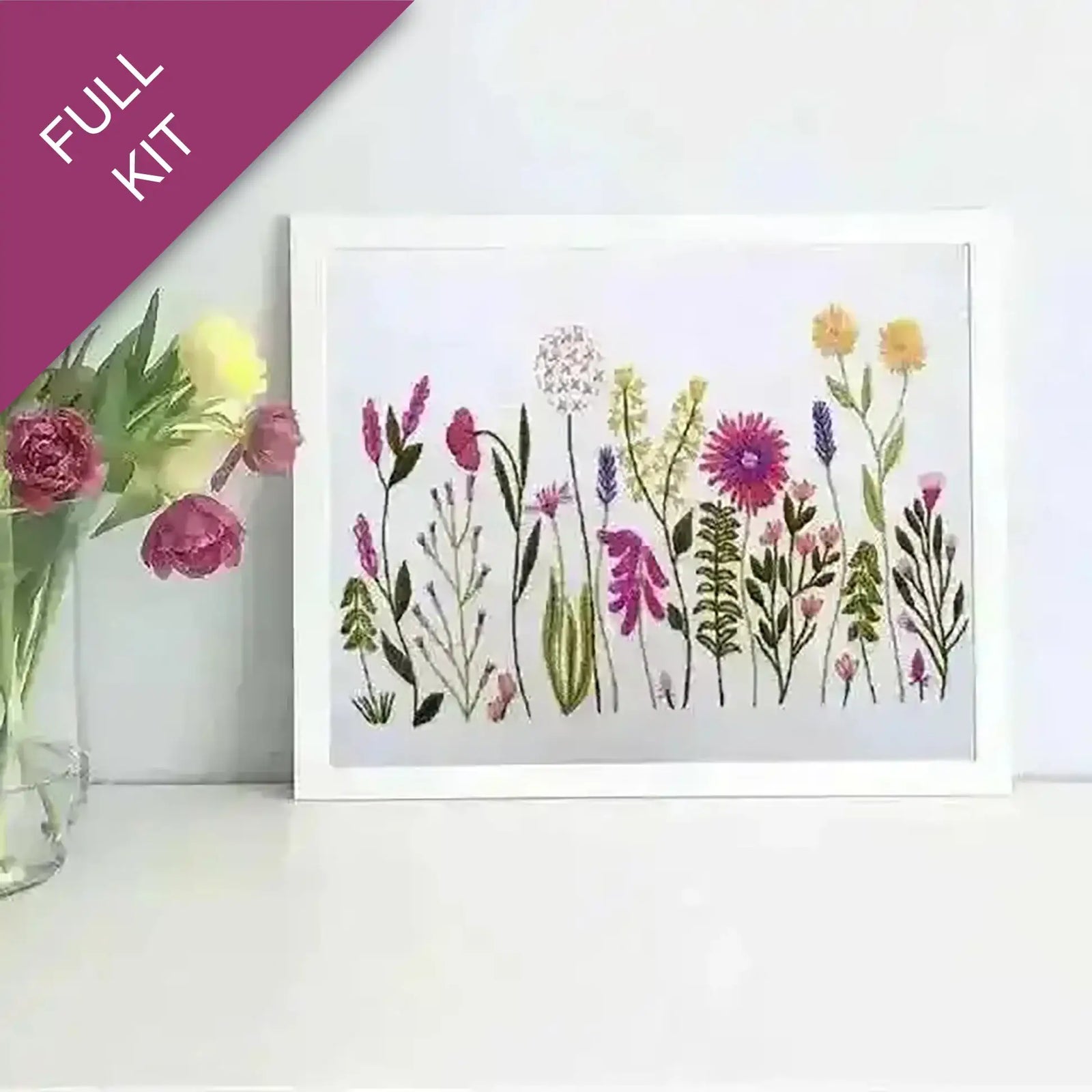 Framed artwork of colorful flowers next to a vase with real flowers on a white surface.