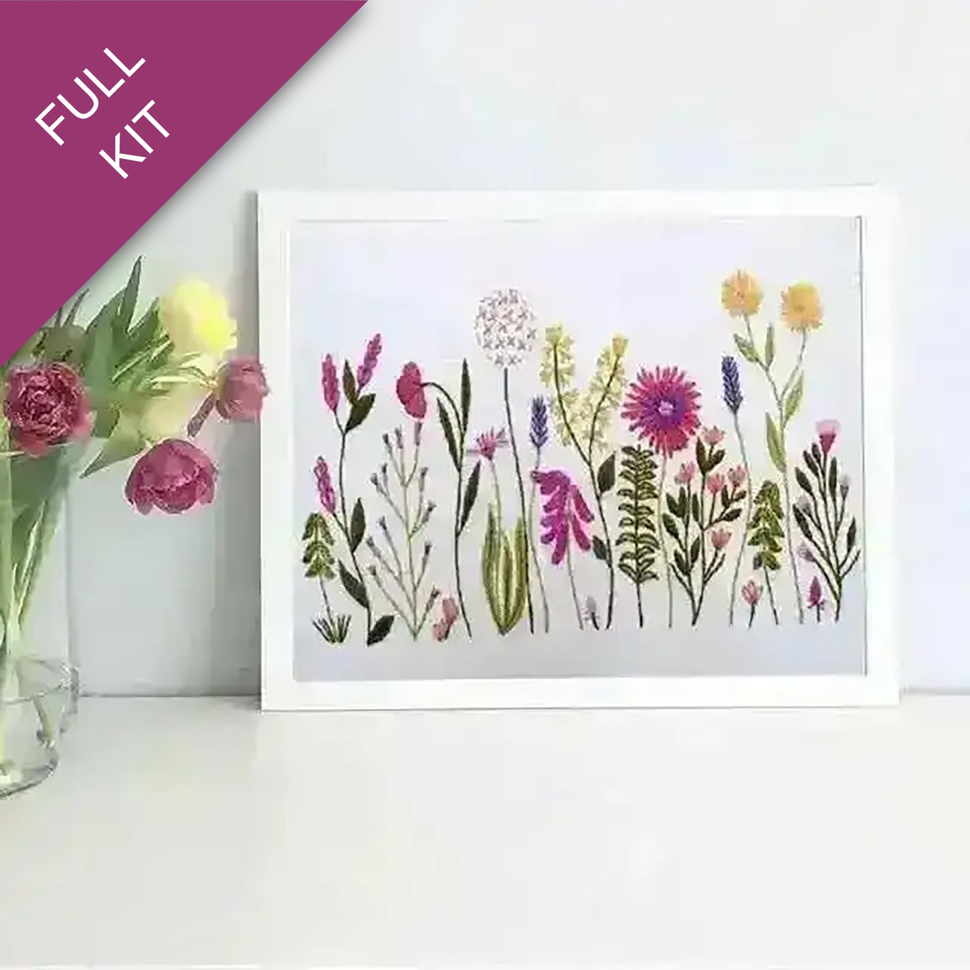 Framed artwork of colorful flowers next to a vase with real flowers on a white surface.