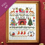 Framed Christmas-themed cross-stitch pattern with reindeer, fireplace, and stockings on a white background.