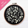 Embroidery hoop with white floral patterns on black fabric, pink PDF pattern label.