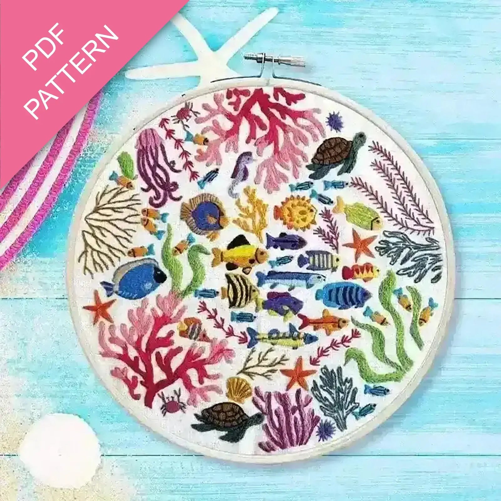 Embroidery hoop with colorful underwater scene including fish and coral on a blue wooden surface.
